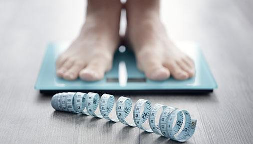 Feet standing on a scale, with a tape measure in front