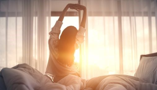 A woman stretching as she gets out of bed