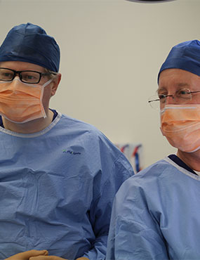 Two surgeons wearing scrubs, caps and face masks.