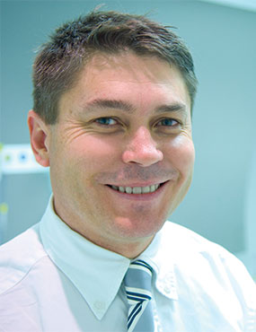 Dr John Fuller, a smiling man wearing a shirt and tie.