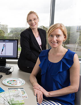 Two seated and smiling staff members, with Healthy Weight clinic brochures.