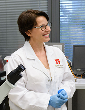 Professor Helen Rizos, smiling, in a labcoat and gloves.
